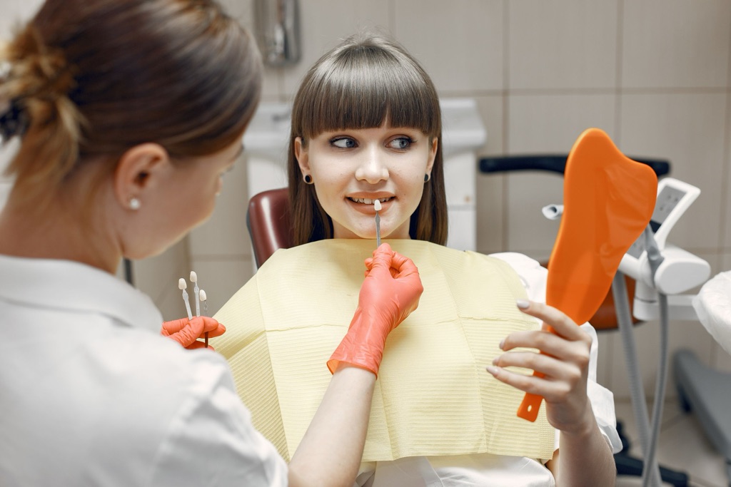 Dentista revisando la boca de una paciente joven que se mira en un espejo de mano